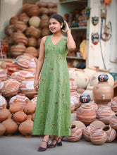 Woman wearing Meadow Bloom Olive Green Cotton Maxi Dress featuring gingham checks, floral motifs, V-neck design, and flowy A-line silhouette in breathable cotton fabric.