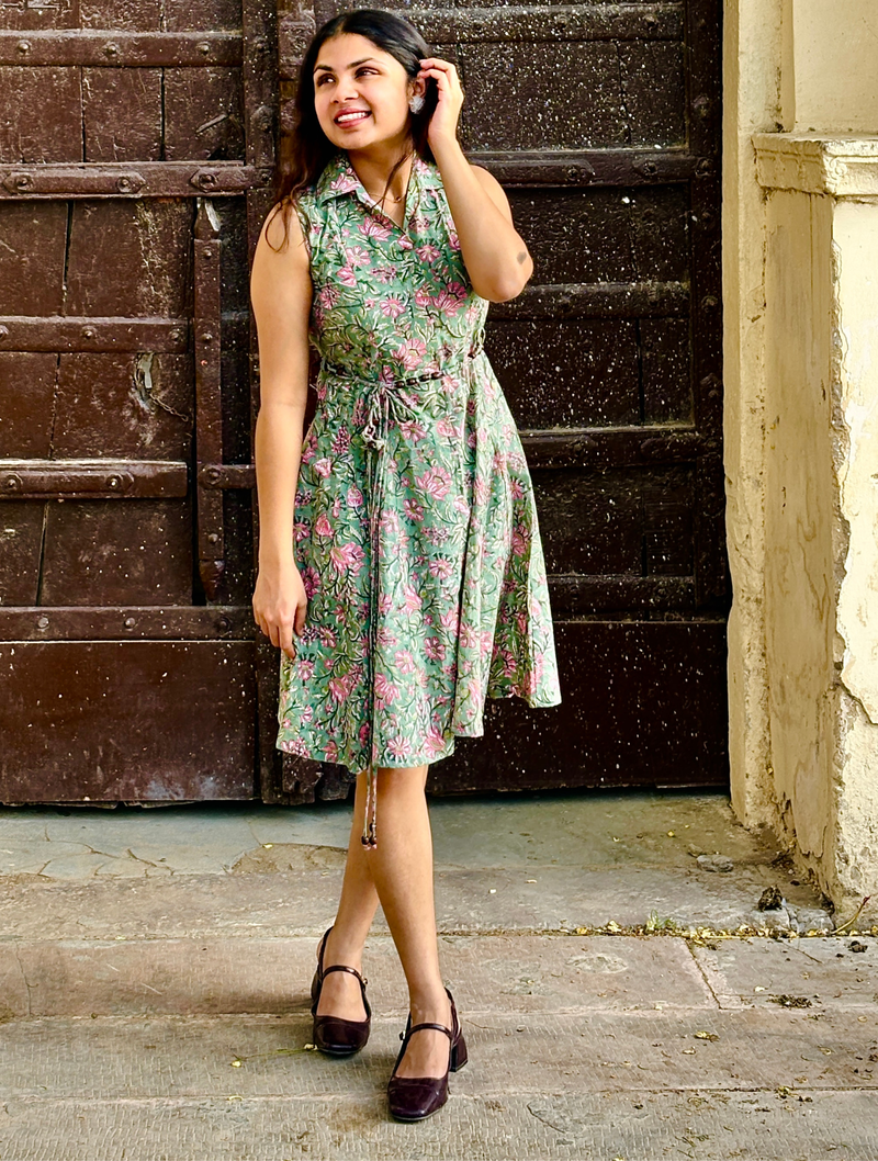 Woman wearing a mint green floral sleeveless A-line dress with a collar neck, adjustable waist tie-up, and knee-length silhouette in an outdoor setting.