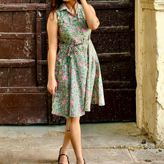 Woman wearing a mint green floral sleeveless A-line dress with a collar neck, adjustable waist tie-up, and knee-length silhouette in an outdoor setting.