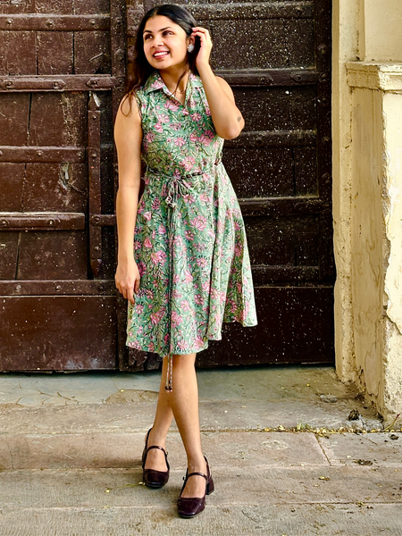 Woman wearing a mint green floral sleeveless A-line dress with a collar neck, adjustable waist tie-up, and knee-length silhouette in an outdoor setting.