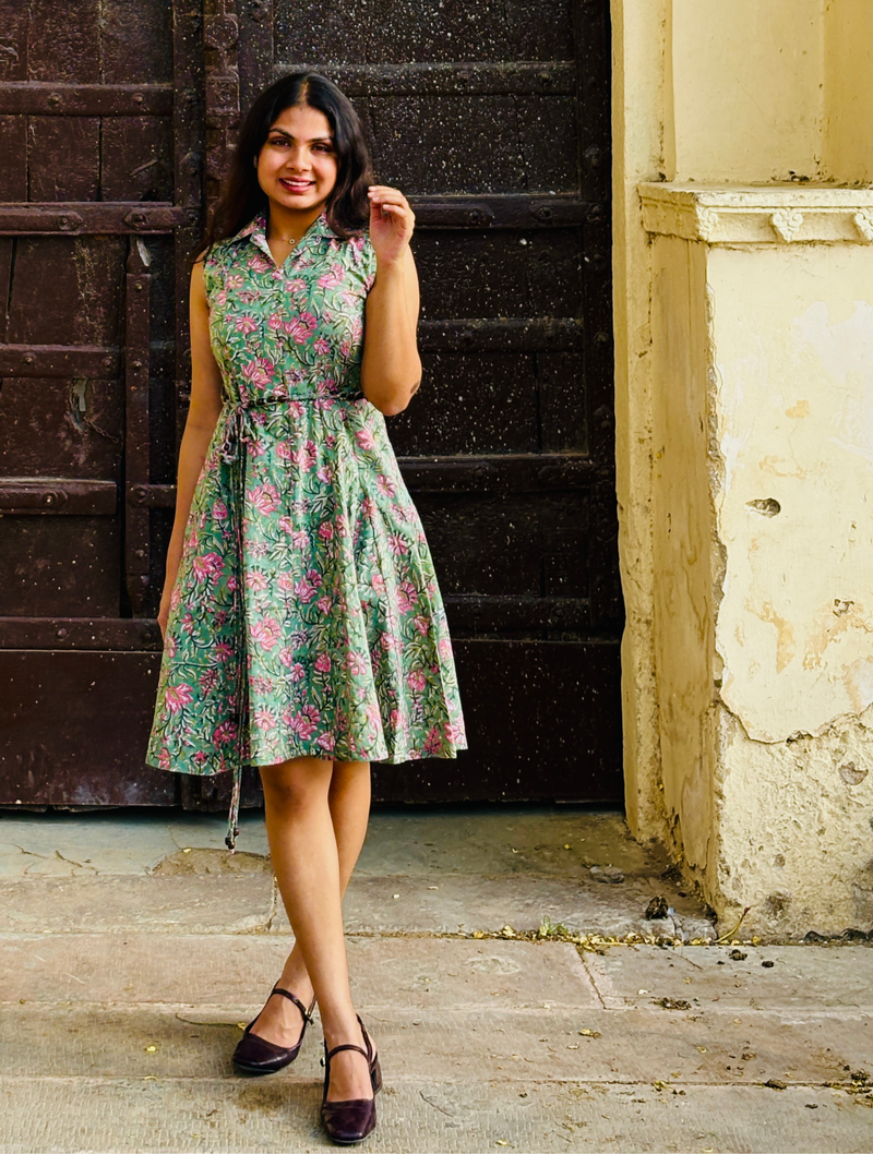 Woman wearing a mint green floral sleeveless A-line dress with a collar neck, adjustable waist tie-up, and knee-length silhouette in an outdoor setting.