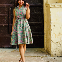 Woman wearing a mint green floral sleeveless A-line dress with a collar neck, adjustable waist tie-up, and knee-length silhouette in an outdoor setting.