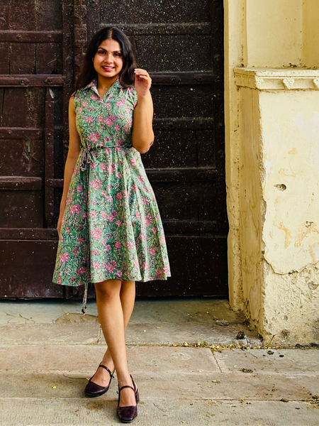 Woman wearing a mint green floral sleeveless A-line dress with a collar neck, adjustable waist tie-up, and knee-length silhouette in an outdoor setting.