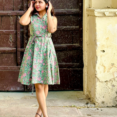 Woman wearing a mint green floral sleeveless A-line dress with a collar neck, adjustable waist tie-up, and knee-length silhouette in an outdoor setting.