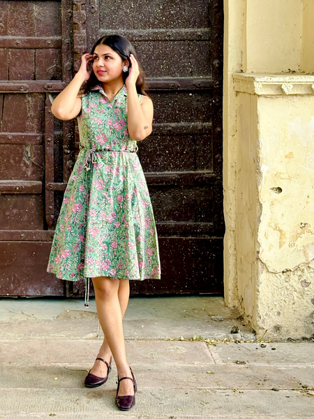 Woman wearing a mint green floral sleeveless A-line dress with a collar neck, adjustable waist tie-up, and knee-length silhouette in an outdoor setting.