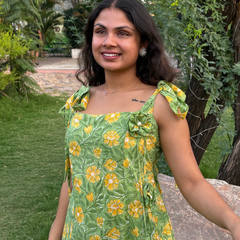 Woman wearing a green floral A-line dress with a square neckline, adjustable tie-up shoulder straps, and knee-length silhouette in a garden setting.